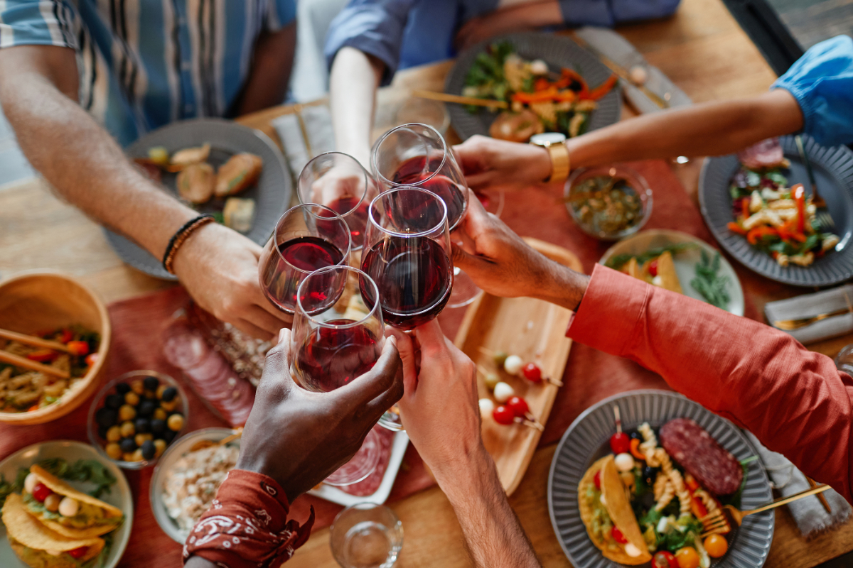 glassess and food on a table, hands holding the glasses
